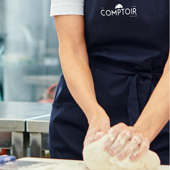 People learning to bake in Comptoir Bakeries workshop with blue aprons on. 