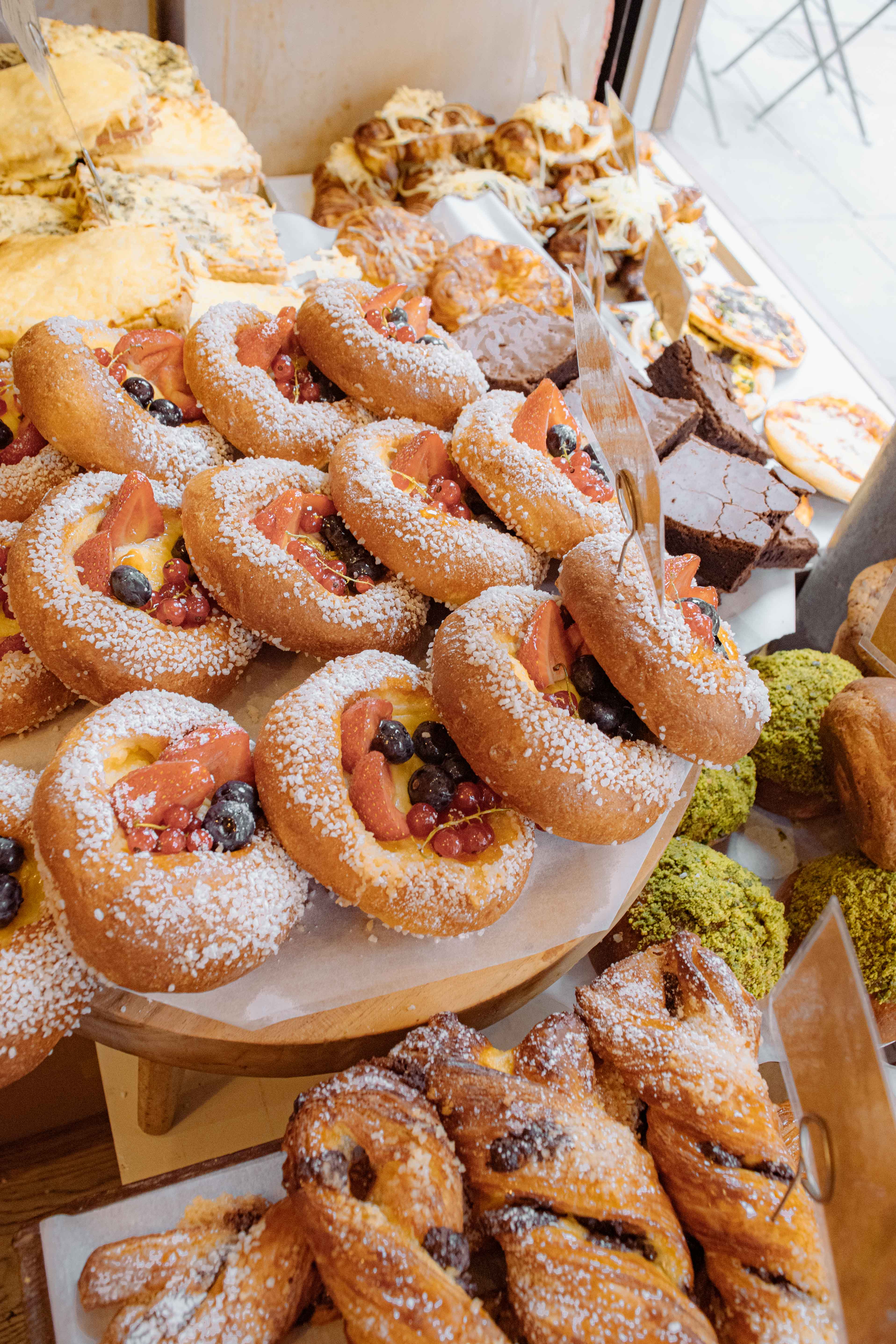 Assortment of freshly baked pastries topped with powdered sugar, berries, and sliced fruit at Bermondsey, including fruit danishes, brownies, and matcha buns.