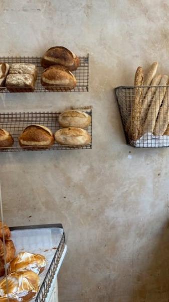 Artisan bread display with crusty baguettes and rustic sourdough loaves on wire shelves against a textured wall at Bermondsey bakery