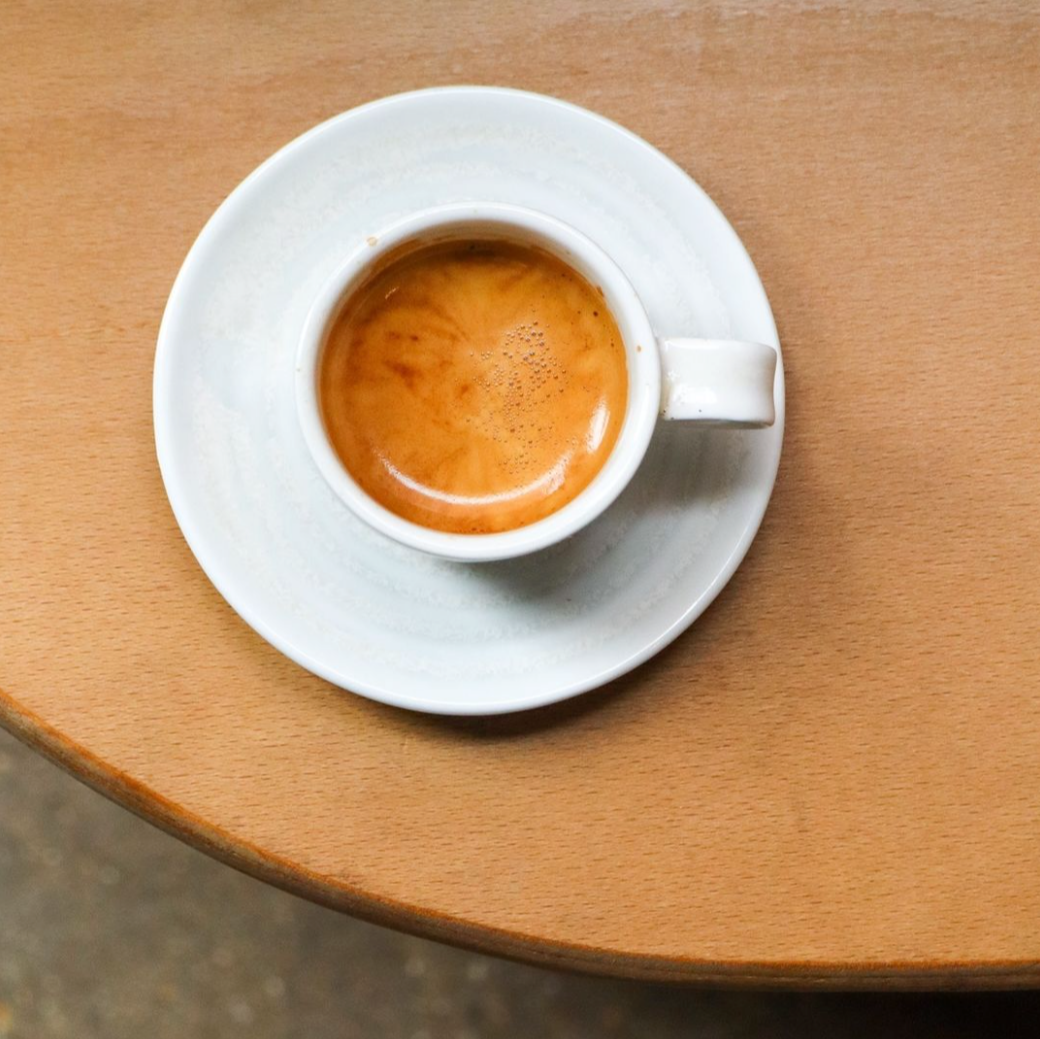 Single shot of espresso served in a white ceramic cup on a wooden table at Comptoir Bakery café.