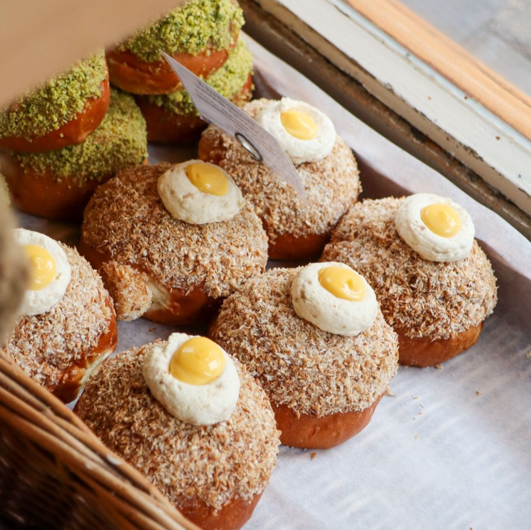 Assortment of filled brioches topped with coconut flakes and lemon cream at Comptoir Bakery, displayed in a wicker basket by the window.